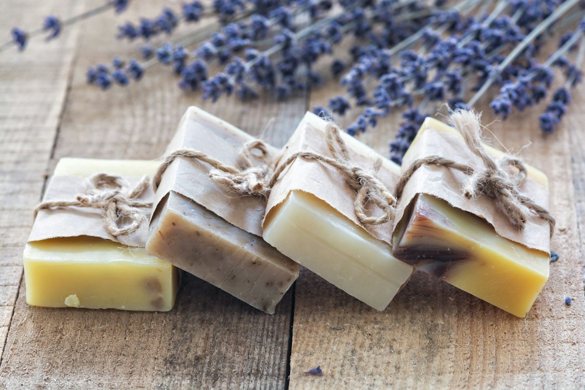 Four bars of soap wrapped in paper and tied with string on wood, lavender in the background